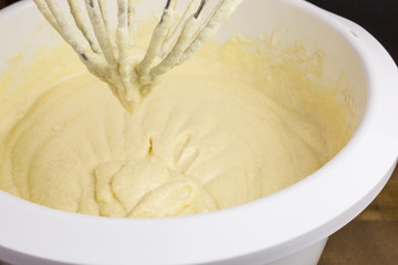 cake batter of butter, eggs, sugar, milk and flour in  a mixing bowl, focus on batter dripping from the beater