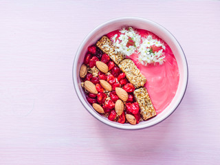 Beautiful flowers, berry smoothie, muesli with nuts, dry berries and pieces of banana in a plate on a stylish, pink table. Healthy and delicious food