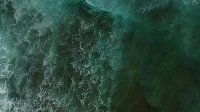 Aerial view of ocean waves and brown rocks in the coastline. Waves hit the shoreline.