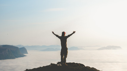 Young man stand on top of mountain top with hands raised in the air. Success and risk concept.