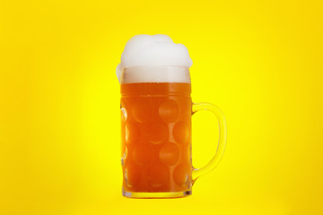 Mug of beer close-up with froth over yellow background