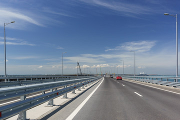 Fototapeta na wymiar Red car rides on the Crimean bridge in the direction of the city of Kerch. Sunny day
