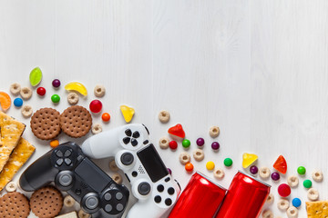 black and white modern gamepads on a white wooden background among sweets, biscuits and cans of...