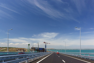 Fototapeta na wymiar Red Car rides on the Crimean bridge across the Kerch Strait. On the left is the construction of the railway bridge