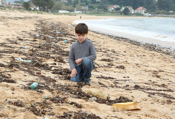 niño triste en la playa mirando la arena llena de plásticos