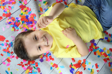 ni&ntilde;o feliz tumbado en el suelo rodeado de confeti de colores