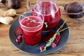 Beet smoothie in a glass and a jug. Thyme and beetroot pieces are around