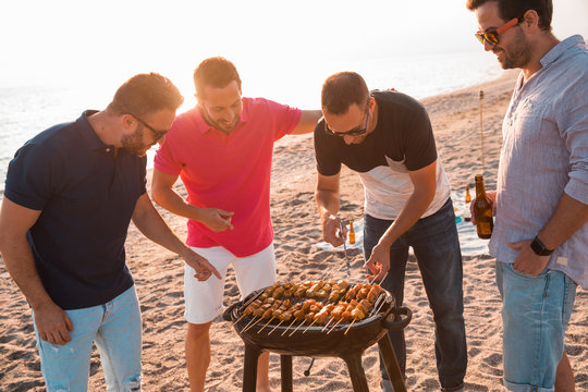 group of young men preparing a barbecue on the beach at sunset. Summer time concept