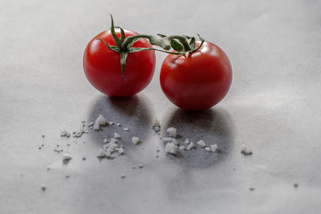Zwei rote Tomaten mit grünem Stengel und Salz auf grauem Beton Hintergrund