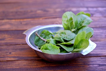 Fresh spinach leaves in a metal bowl on a wooden table. The concept of a healthy diet.