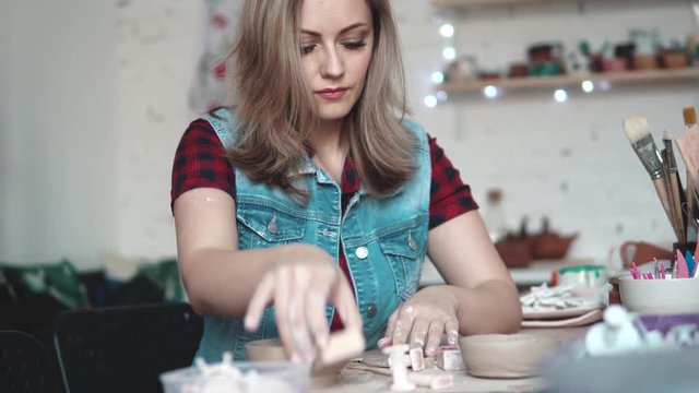 attractive young Caucasian woman spends time behind a creative hobby. the girl enthusiastically sculpts a plate of clay in the workshop