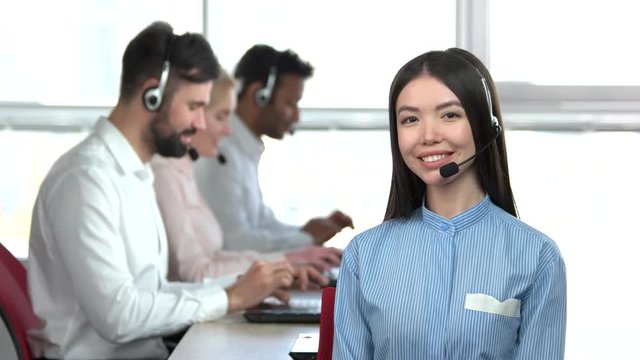 Cheerful asian office girl with co-workers background. Adorable young asian woman in office in front of colleagues.