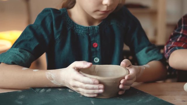 child is making a plate of clay. a lesson in pottery. little girl makes patterns on a clay stamp