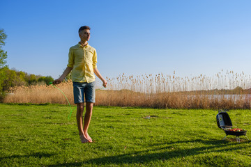 Young caucasian boy is doing workout with jumping rope on green grass lawn