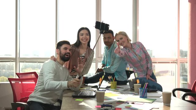 Co-workers taking photo usind selfie stick and playing the ape. Group of office workers taking picture of themselves with smartphone using selfie stick.