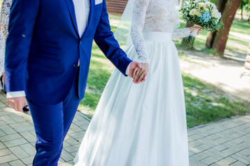 Obraz na płótnie Canvas holding hands bride and groom love wedding bouquet blue suit and white dress