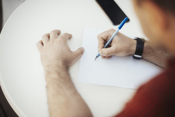 Young attractive man is writing note at the paper.