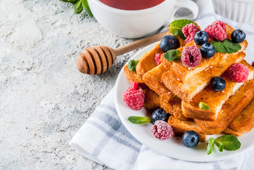 Healthy summer breakfast, baked french toasted bread sticks with fresh berry and honey, morning light grey stone background copy space