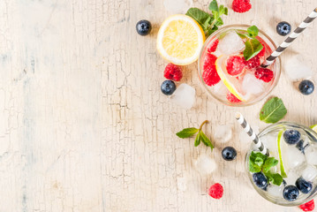 Various berry lemonade or mojito cocktails, fresh iced lemon lime raspberry blueberry infused water, summer healthy detox drinks light background copy space above