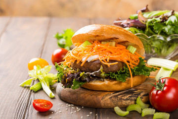 Delicious bagel burger with beef,tomato, carrot, fresh salad served on wooden board. Healthy junk food concept with copy space.