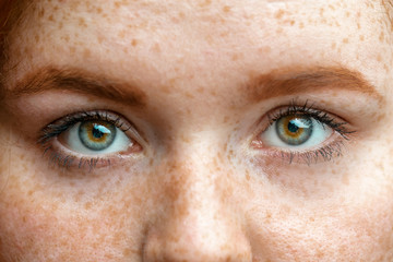 Close up eyes of young red ginger freckled woman with perfect healthy freckled skin, looking at...