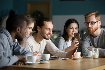 Multi-ethnic group of young friends talking and using smartphones apps on wifi in cafe, happy millennial people having fun with phones sharing coffee house table enjoying meeting in public place