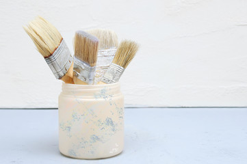 Old dirty brushes for plaster in a plastic jar on a white stucco background.