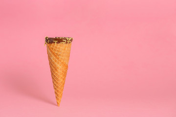 funny creative concept of close up empty wafer cone with chocolate glaze and colorful sprinkles over pastel pink background