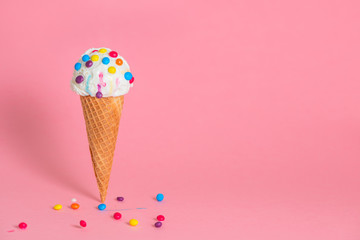 summer funny creative concept of wafer cone with melting ice cream covered and strewed colorful chocolate confetti on pink background