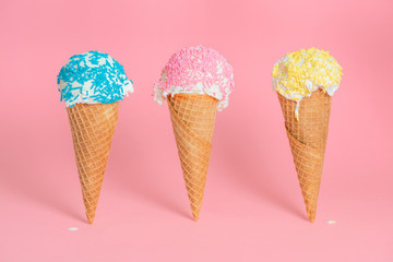 funny creative concept of close up three wafer cups with melting ice cream and colorful sprinkles over pastel pink background