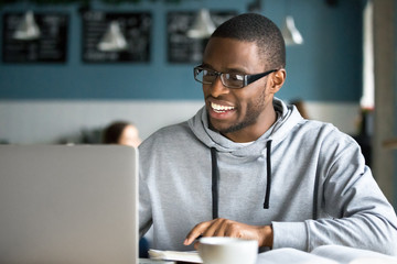 Smiling millennial african american casual man in glasses working with apps or communicating online...