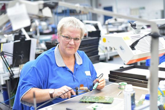 Portrait &auml;ltere Frau in einer Fabrik zur Montage von moderner Elektronik am Arbeitsplatz // older woman in a factory to assemble modern electronics at the workplace