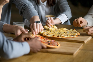 Obraz na płótnie Canvas Hands of diverse people taking pizza slices from wooden board dining together, multiracial friends or colleagues sharing meal having lunch in cafe restaurant, italian pizzeria concept, close up view