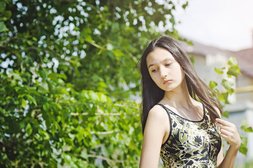 Beautiful teen girl brunette with long hair on a background of green trees.