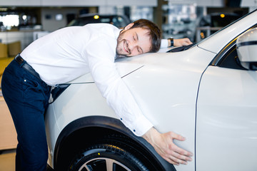 Happy businessman hugging his new car in showroom