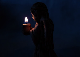 angel holds a burning candle in the dark. background religion, prayer.