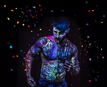 Young man painted in fluorescent paint on face and muscular torso, in studio shot with UV light