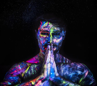 Young man painted in fluorescent paint on face and muscular torso, in studio shot with UV light