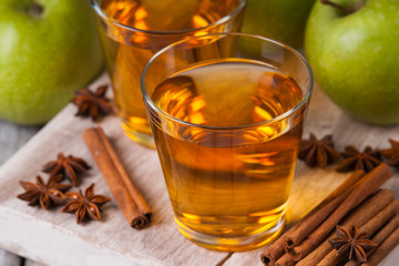 Apple juice in glasses, spices and apples on wooden cutting table 