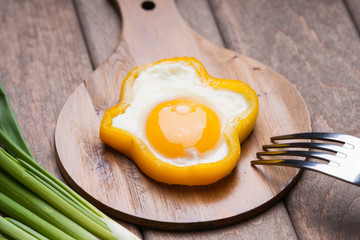 Bell pepper egg ring on a cutting wooden board, fork and green onion 