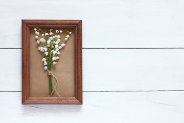 Small bouquet of lilies of the valley in a wooden frame on a white wooden background