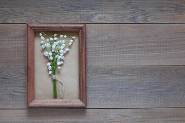 Small bouquet of lilies of the valley in a wooden frame on a wooden background