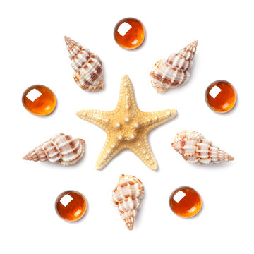 Pattern in the form of a circle made of shells, starfish and orange glass pebbles isolated on white background