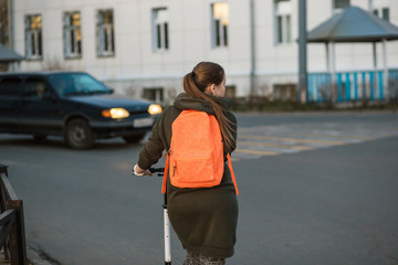 Woman with kick scooter crossing the busy street along the pedestrian crossing