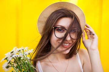 Happy hipster girl wearing glasses and hat with flowers against yellow background. Summer outfit. CLose up
