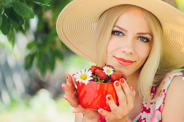 young tender blonde woman with strawberries in a bowl, in a green garden a summer sunny day, warm summer toning of an image, self-care and a healthy lifestyle