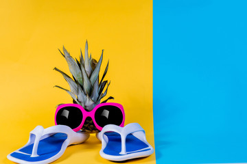 Blue Flip-flops, sandals, Sunglasses and pineapple. Summer is coming concept. Minimal style, minimalist photography. Yellow, pink and blue pastel colors background.