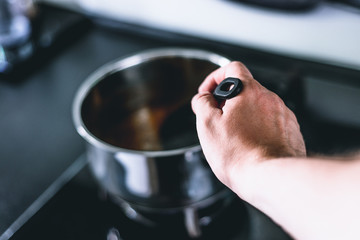 A male hand mixing a soup in a pot. The man fills his household duties, cooks and prepares food, dinner.