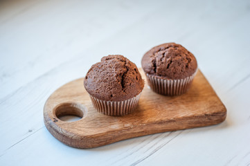 Two chocolate muffins on a wooden board against a white background. Process of cupcakes preparation. Homemade  Cupcakes. Close up, soft focus.