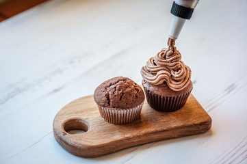 Decorating chocolate muffin with chocolate cream on a white wooden table. Process of cupcakes preparation. Homemade cupcake. Copy space. Soft focus.